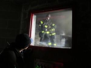 A photo of firefighters training in the "burn room", as seen from the control room.